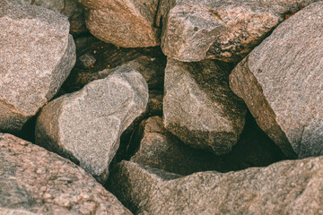 Large large stones of different shapes made of granite with a slight orange tint, close-up, lie next to each other, forming a shadow between them. Some stones have a variety of patterns.
