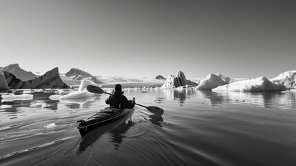 Man kayaking in kayak among icebergs in scenic glacial lagoon in black and white
