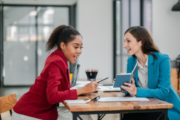 Two professional women engaged in a productive discussion at a contemporary office, working on laptops and taking notes.