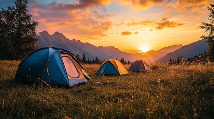 A row of tents set up in a scenic meadow, with the first light of dawn breaking over the mountains, signaling the start of a new day.