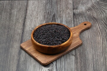 pile of black rice in a wooden bowl on a wooden table close-up