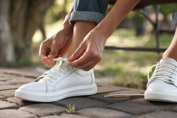 Naklejka premium Woman tying shoelace of white sneaker outdoors, closeup