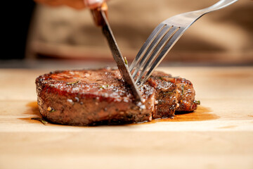 A person is cutting a piece of tenderloin meat with a knife on a wooden cutting board