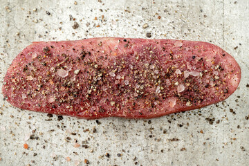 A slab of sirloin meat is covered in salt and pepper