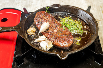 A piece of sirloin meat is cooking in a pan with garlic and herbs
