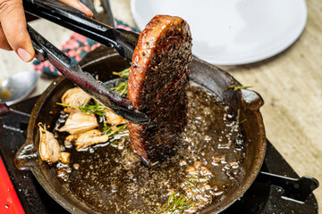 A person is cooking a sirloin steak in a pan with garlic and herbs