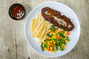 A plate of food with a piece of sirloin meat, vegetable mix, and french fries