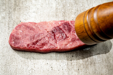 A piece of sirloin meat is being flavored with a pepper mill