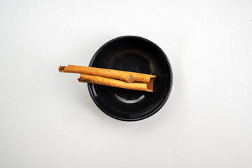A bowl of cinnamon sticks sits on a white background