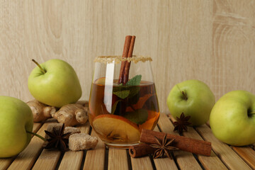 Glass with cider, apples and spices on wooden background
