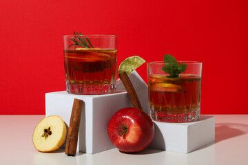 Glasses with apple cider, apples and cinnamon sticks on red background