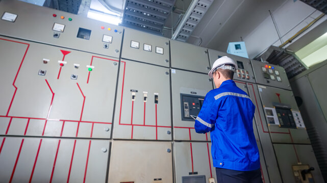Electrical engineers check the operation of the main electrical control panels and switches, record values ​​on tablets, electrician inspect the electrical systems in the factory.