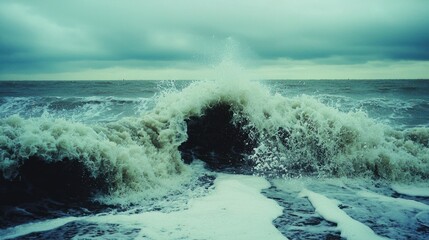 Fototapeta premium A Large Wave Breaking on the Shore with a Cloudy Sky Overhead