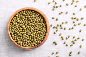 Mung beans, green gram in a wooden bowl on linen fabric. Dried seeds of Vigna radiata, a member of the legume family Fabaceae, used as an ingredient in both savoury and sweet dishes in Asian cuisine.
