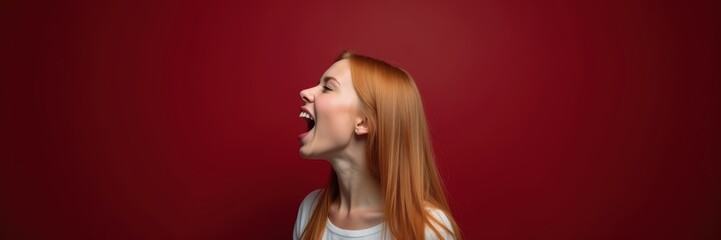 Fototapeta premium A joyful young woman with long red hair expresses excitement against a vibrant red background, capturing the essence of happiness and energy.