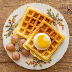 Belgian waffles served with sunny side up egg and fresh grapes on ceramic plate over wooden...
