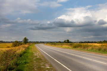 A road with a few trees in the background and a cloudy sky