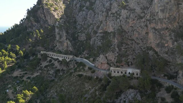 Aerial view of scenic MA-10 roads tunnels winding through majestic mountains and lush greenery, Estellencs, Spain.