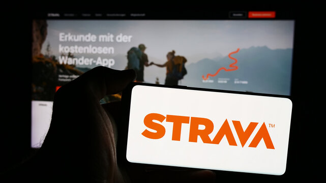 Stuttgart, Germany - 08-20-2024: Person holding mobile phone with logo of American fitness network company Strava Inc. in front of business web page. Focus on phone display.
