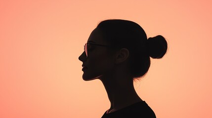 Silhouette of a woman in profile with a bun hairstyle against a peach background.