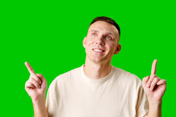 Young Man Pointing Upward While Smiling Against a Bright Green Background