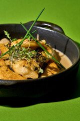 A close-up of a cast iron skillet filled with golden-brown, baked varenyky. The varenyky are garnished with fresh herbs on green background.
