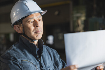 Supervisor of a manufacturing site wearing a white helmet with a machine tool in the background.