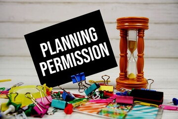 Planning Permission text on paper card with hourglass and stationary on wooden background