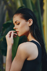 Attractive woman in black swimsuit standing in front of palm tree holding hand to her face