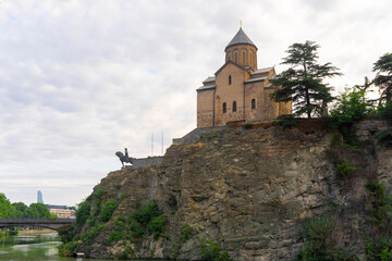 Fototapeta premium Metekhi Virgin Mary Assumption church and Vakhtang Gorgasali statue on the rock. Mtkvari (Kura) river and bridge