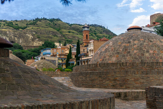 Domes of sulfur baths and Tbilisi Mosque (Juma Mosque) in the downtown. Mountains and sky with clouds in the background