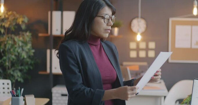 Slow motion portrait of Middle Eastern businesswoman reading document then looking at camera and smiling standing in office. Business and employee concept.