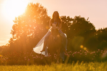 A young woman wearing a dress and her haflinger horse mare in front of a beautiful summer sunset...