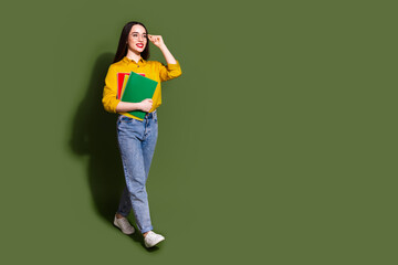 Full length photo of cheerful pretty lady dressed yellow blouse holding book walking empty space isolated khaki color background