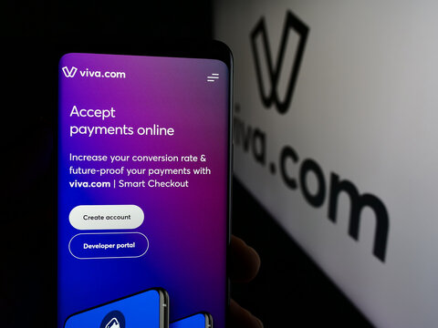 Stuttgart, Germany - 08-22-2024: Person holding cellphone with web page of Greek payment company Viva Payments (Viva.com) in front of logo. Focus on center of phone display.