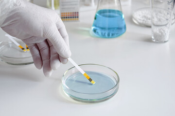A scientist in a chemical laboratory takes measurements of the acid-base balance of a liquid in a Petri dish.