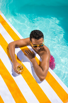 Smiling man with drink leaning on towel at poolside