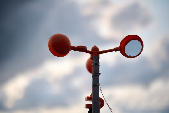 A red anemometer spins against a cloudy Hong Kong sky, measuring wind on a pole, blending technology with natural weather.