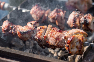 Pork kebab in the country in nature. May holidays. Pork kebab on skewers. The process of cooking meat on the grill with smoke, close-up.