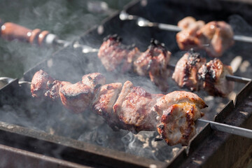 Pork kebab in the country in nature. May holidays. Pork kebab on skewers. The process of cooking meat on the grill with smoke, close-up.