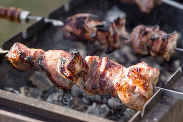 Pork kebab in the country in nature. May holidays. Pork kebab on skewers. The process of cooking meat on the grill with smoke, close-up.