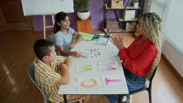 High angle view of cheerful female Hispanic teacher conducting lesson of speech therapy to diverse schoolkids
