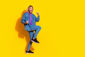 Full length portrait of nice young man raise fists empty space wear denim jacket isolated on yellow color background
