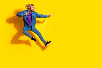 Full length portrait of nice young man jump fight empty space wear denim jacket isolated on yellow color background