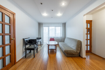 Old Retro Classic Style Living Room Interior. Couch Sofa, Wooden Floor, Coffee Table and Wardrobe In Background. White Walls and Ceiling. Bright Lamp.