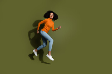 Full length photo of adorable lovely girl wear orange jumper jumping high hurrying empty space isolated khaki color background