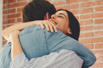 Happy couple embracing at home, celebrating the end of an argument or an anniversary. The young woman reacts joyfully to a proposal, symbolizing gratitude, love, and commitment in their relationship