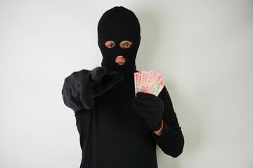 Dangerous young Adult black masked robber is holding a bunch of indonesian money after stealing from his victim.