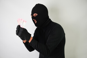 Dangerous young Adult black masked robber is holding a bunch of indonesian money after stealing...