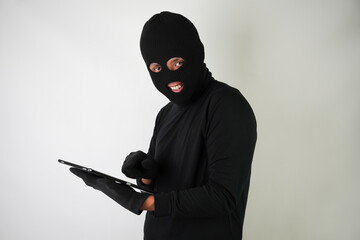 Young Adult black masked robber is holding digital tablet with blank green screen and he calling his target victim with terror. Concept for hacking, scamming, phishing.
